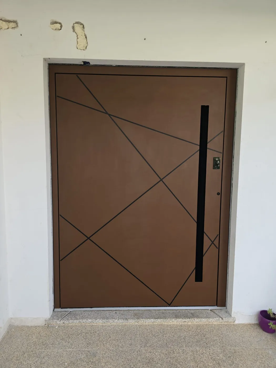 Porta de entrada lacada em tom bronze com frisos geométricos pretos e puxador em barra