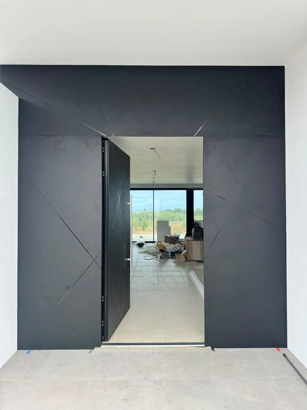 Porta pivotante preta de grandes dimensões, com frisos diagonais, integrada num revestimento da mesma cor